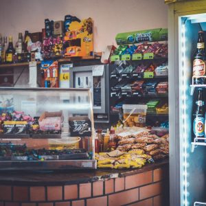 A well-stocked convenience store counter with snacks, drinks, and a refrigerator showcasing beverages.